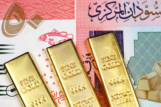 Three small gold bars close up with a fifty Sudanese pound bank note in macro.